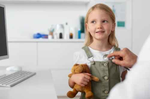 A young girl holding a teddy bear is examined by a Paediatrician